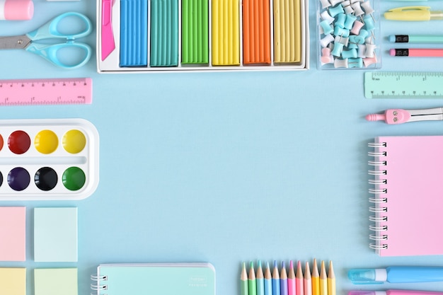 A frame of school supplies in pastel colors on a light blue surface, space for text