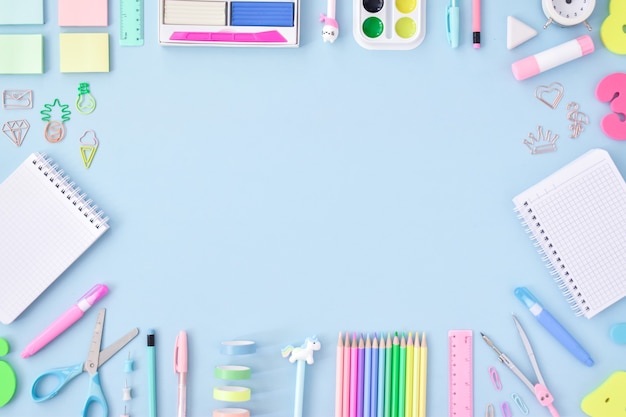 A frame of school supplies in pastel colors on a light blue surface