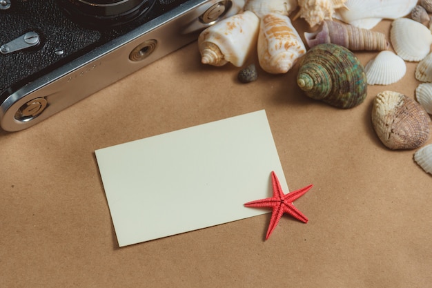 Frame of seashells and photo camera on light background with blank card