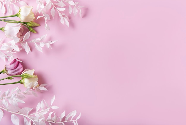 Frame of white branches with leaves and flowers on a pink background