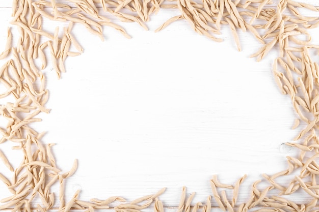 Frame of whole grain wheat raw apulian pasta called Pizzarieddi or maccaruni on a on white wooden table. Fresh maccheroni typical dish of Puglia, Salento Italy. Italian homemade pasta background