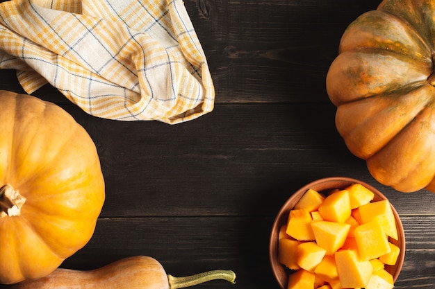 A frame of whole pumpkins of different sizes and a plate with pumpkin slices on a black wooden background. Kitchen towel. Copy space. Top view.