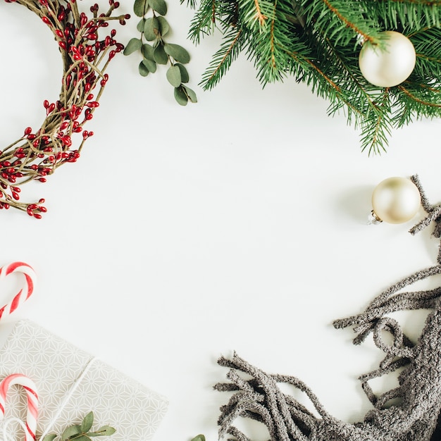 Рама с копией пространства из рождественских украшений: венок, конфеты, одеяло, эвкалипт на белой поверхности. Плоская планировка, вид сверху