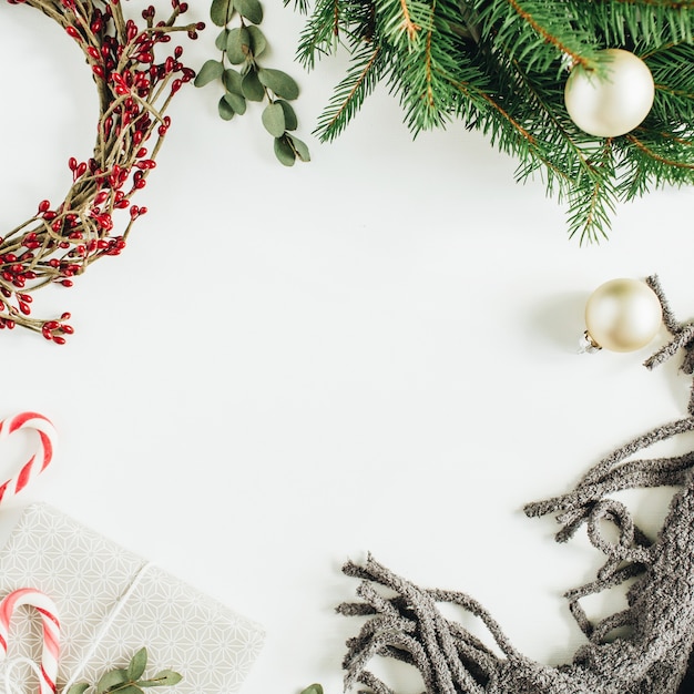 Frame with copy space made of Christmas decorations: wreath , candies, blanket, eucalyptus on white surface. Flat lay, top view