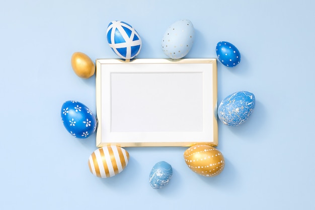 Frame with gold decorated easter eggs with copy space for text on blue surface. Minimal Happy Easter concept. Top view, flatlay.