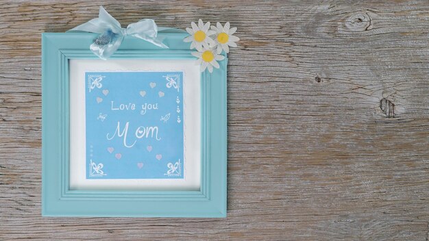 Photo frame with hand lettering text in english love you mom wood background flowers of the magerite