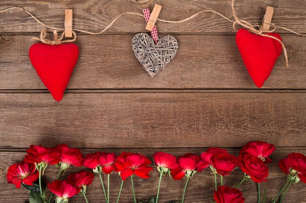 Frame with roses and red hearts on wooden background valentines day