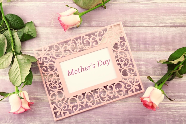 Frame with text MOTHER'S DAY and flowers on wooden background