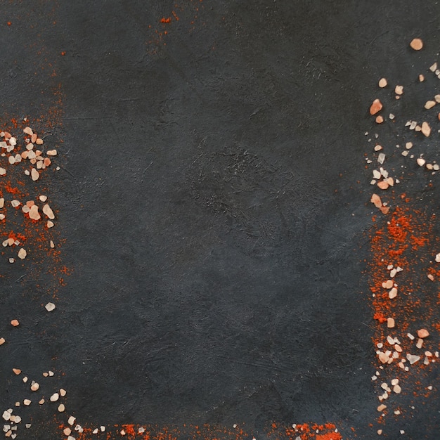 Framed empty space dark background chunks of salt and red pepper or paprika spice condiments rough textured surface food preparing and cooking concept