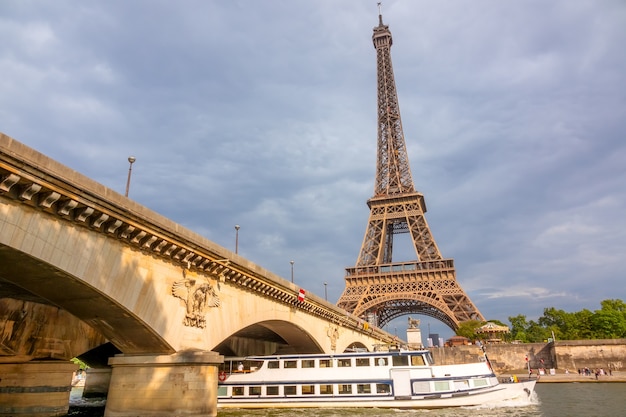 フランス。太陽に照らされたイエナ橋の下の遊覧船。曇り空を背景にしたエッフェル塔