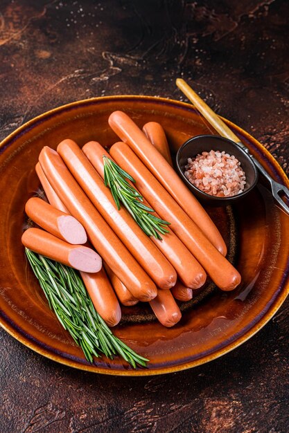 Frankfurter raw sausages in a rustic plate with herbs. Dark background. Top view.