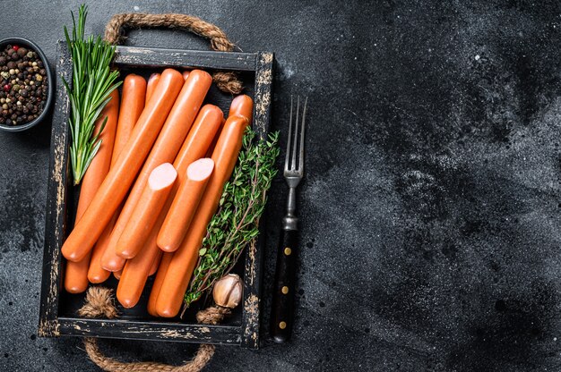 Frankfurter sausages in a wooden tray with herbs. Black background. Top view. Copy space.