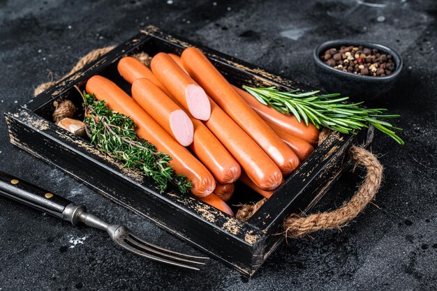 Frankfurter sausages in a wooden tray with herbs. Black background. Top view.