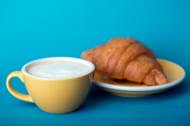 Frans ontbijt. mooie koffie gele kop cappuccino met croissant op blauwe achtergrond