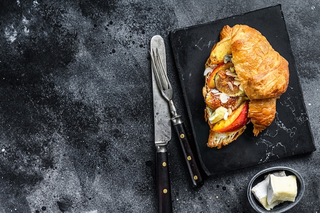 Franse croissant met bree-kaas, perzik en vijgen. Zwarte houten achtergrond. Bovenaanzicht. Kopieer ruimte.