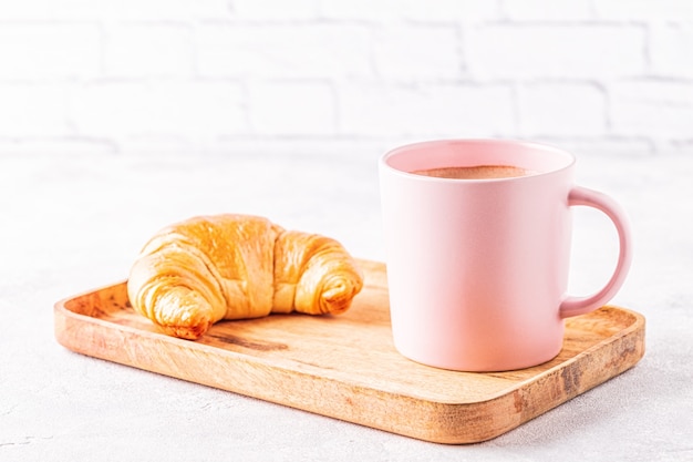 Franse croissants en kopje koffie op een houten dienblad.