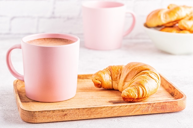 Franse croissants en kopje koffie op een houten dienblad.
