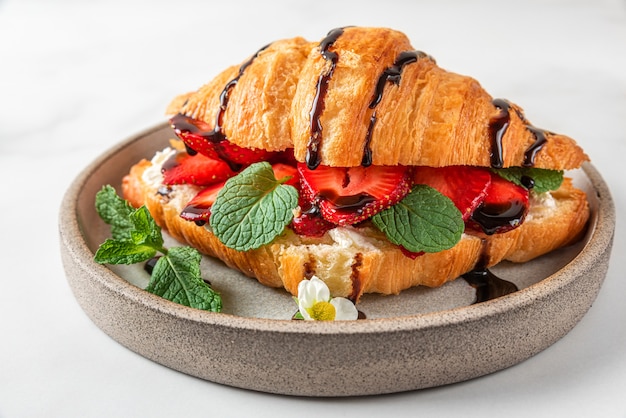 Franse croissantsandwich met verse aardbeien, roomkaas, munt en chocoladesaus op witte achtergrond