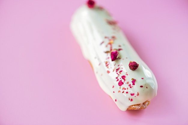 Franse desserteclairs of soesjes met witte chocoladeglazuur met rozensmaak, op een roze achtergrond. Gebakcakes met custard, rozenroom en topping. Zachte selectieve focus.