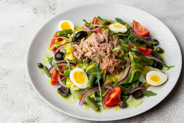 Franse salade nicoise met tonijn ei sperziebonen tomaten olijven sla uien en ansjovis op een witte achtergrond gezonde voeding