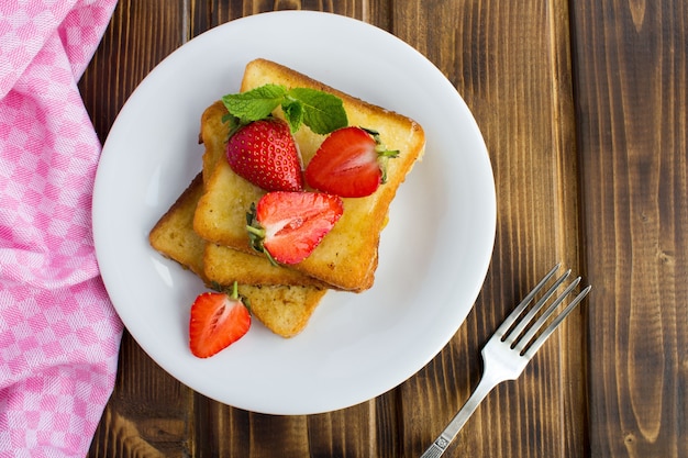 Franse toast met aardbeien in de witte plaat op de bruin houten tafel. Bovenaanzicht. Kopieer ruimte. Close-up.