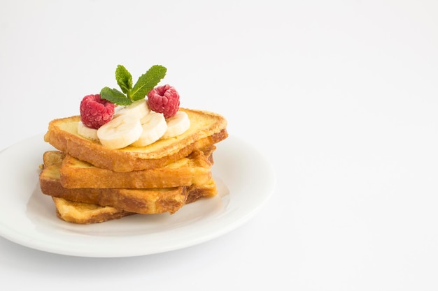 Franse toast met banaan en framboos op de witte plaat op de witte achtergrond. Ruimte kopiëren.