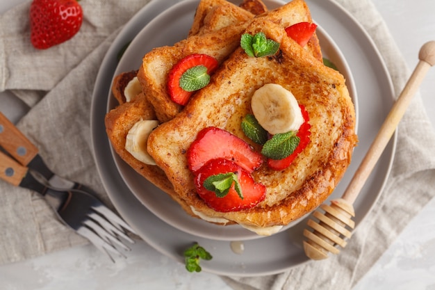 Franse toast met honing, banaan en aardbeien op een grijze plaat. Grijze achtergrond, kopie ruimte, bovenaanzicht.