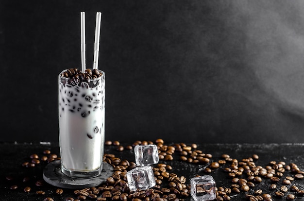 Frappe van ijskoffie met melkconcept in een hoog glas met de rietjes. koffiebonen op donker