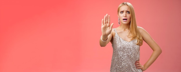 Foto donna bionda insicura infastidita, scontenta, sconvolta, in un vestito scintillante d'argento, estende il palmo eno