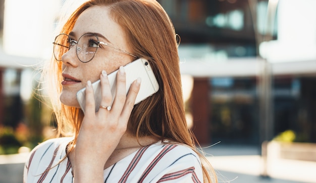 Freckled caucasian entrepreneur with red hair and eyeglasses is having a phone discussion outside