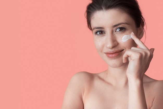 Freckled woman with naked shoulders is posing on a studio wall