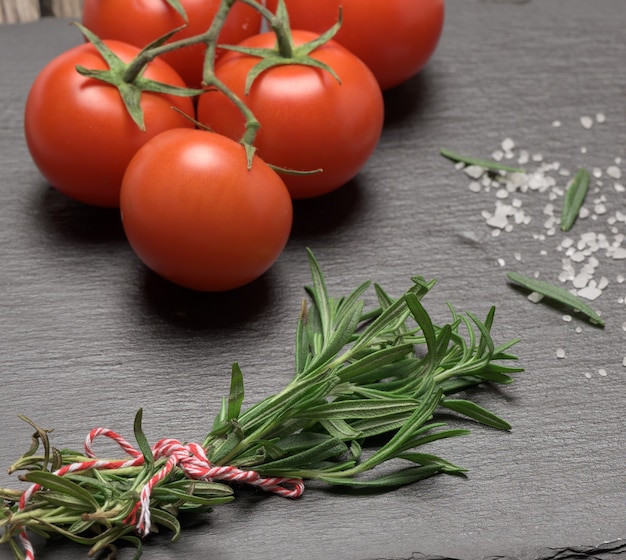 Fred tomatoes and fresh sprig of rosemary with green leaves on a black surface, fragrant seasoning