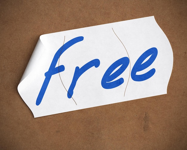 Photo free word hanwritten onto a tearable price tag over a cardboard background, blue color text, white label and brown carton