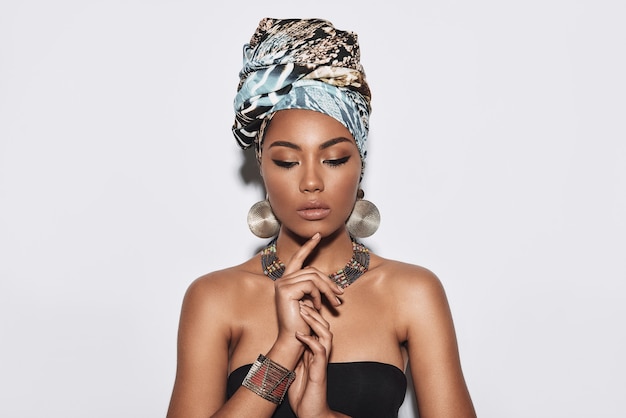 Free your individuality. Attractive young African woman in turban looking down while standing against grey background