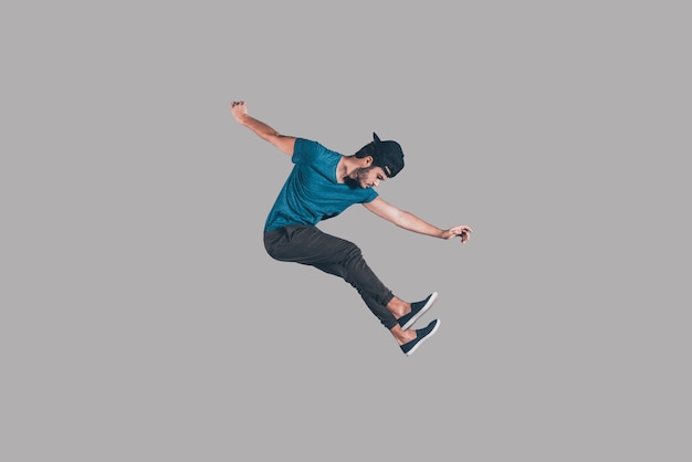 Freedom in every move. Mid-air shot of handsome young man in cap jumping and gesturing against background