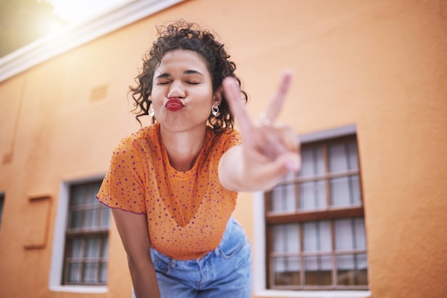 Photo freedom fun and hand peace sign by flirting black woman posing outdoors relax and carefree love positive and peaceful mindset by african american showing finger gesture and kiss in casual fashion