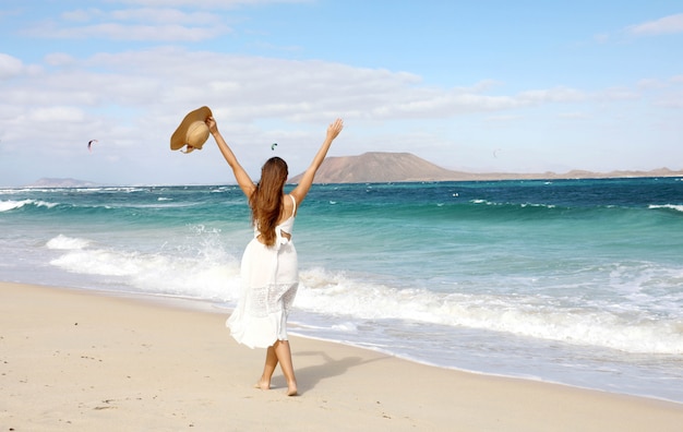 Freedom happy girl enjoying wind with raised arms and people kitesurfering, corralejo dunes beach, fuerteventura, canary islands