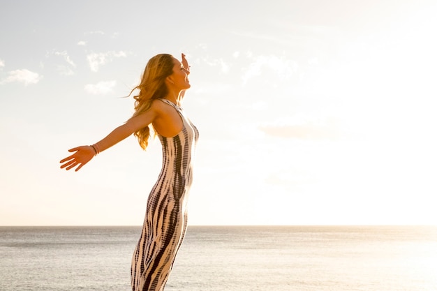 Freedom and joy concept people happy lifestyle with standing and cheerful beautiful young caucasian woman opening arms and enjoying outdoor naure leisure activity - ocean background and sky