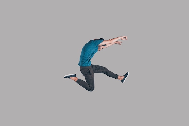 Freedom in moving. Mid-air shot of handsome young man in cap jumping and gesturing against background