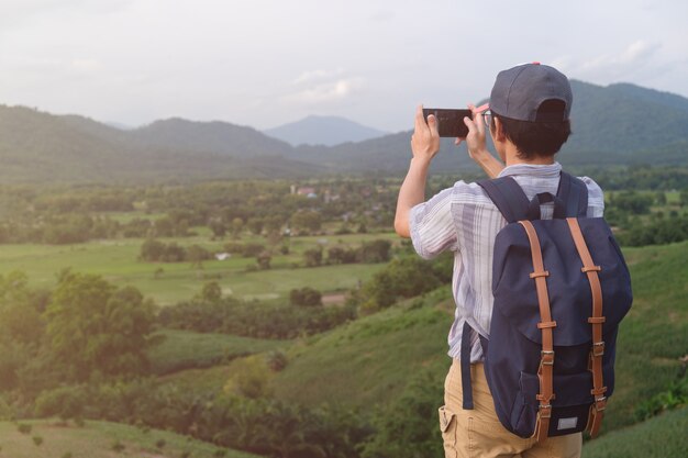 立っている自由旅行者の男。バッグを運ぶ男、電話で写真を撮る