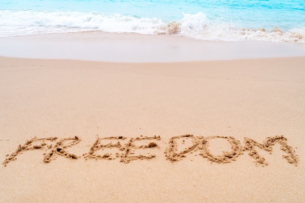 Freedom word hand drawn on sand summer beach.