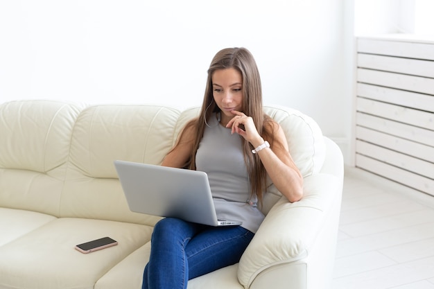 Концепция внештатных и людей - молодая женщина, сидящая на диване и работающая на ноутбуке.
