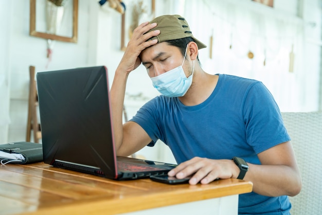 Freelance asian young man wearing face mask working with laptop computer and feeling sad