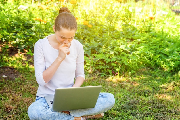 Freelance bedrijfsconcept. Jonge vrouw zittend op groen gras gazon in stadspark bezig met laptop pc-computer. Lifestyle authentiek openhartig studentenmeisje dat buitenshuis studeert. Mobiel kantoor