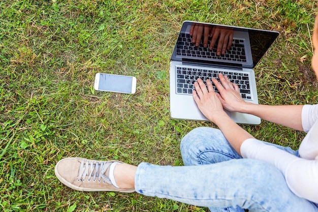 Freelance bedrijfsconcept. Jonge vrouw zittend op groen gras gazon in stadspark bezig met laptop pc-computer. Lifestyle authentiek openhartig studentenmeisje dat buitenshuis studeert. Mobiel kantoor