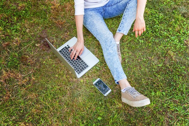 Freelance bedrijfsconcept. Vrouwenbenen op groen grasgazon in stadspark, handen die aan laptop pc-computer werken. Lifestyle authentiek openhartig studentenmeisje dat buitenshuis studeert. Mobiel kantoor