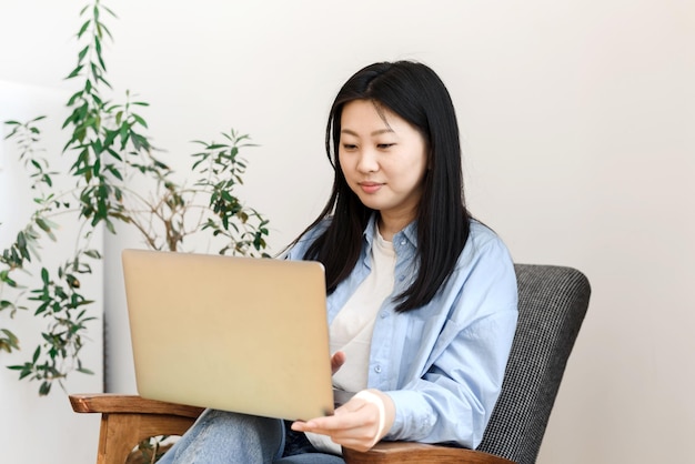 Freelance concept aziatische jonge vrouw zit in een fauteuil met een laptop die thuis werkt