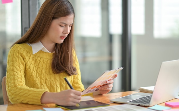 A freelance designer holds a color charger in hand, sketching on a digital tablet.