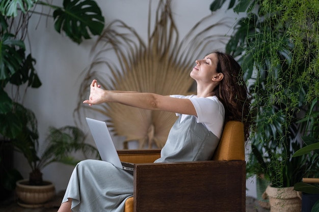 Photo freelance florist girl stretching arms after discussion of indoor garden planting with client online