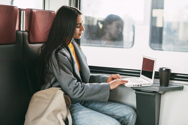 Foto ragazza freelance seduta su un treno con un portatile, tecnologia moderna e networking